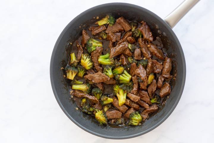 Beef and broccoli florets in a soy based sauce in a skillet.
