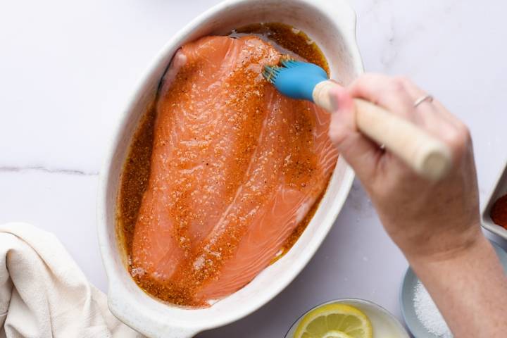 Salmon being brushed with a lemon pepper spice mixture.