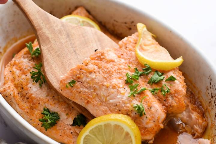 Baked lemon pepper salmon being lifted with a wooden spatula.