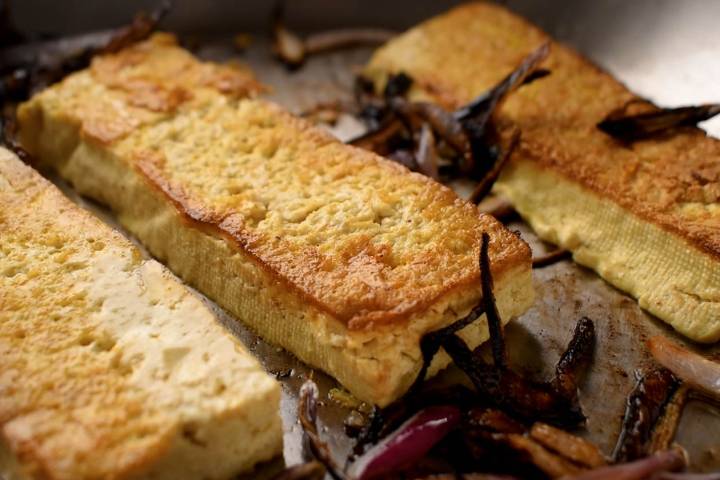 Tofu being pan fried with onions in a skillet.