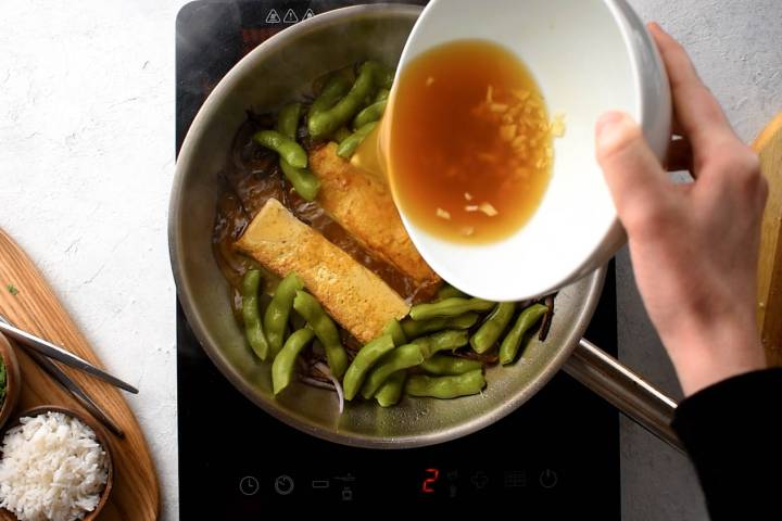 Asian sauce being poured in a pan with tofu and edamame.