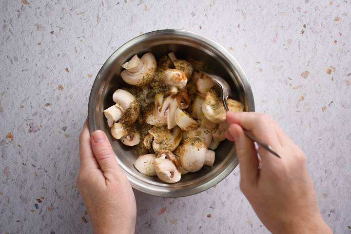 Halved mushrooms in a bowl with olive oil, balsamic vinegar, soy sauce, garlic, thyme, salt, and pepper.