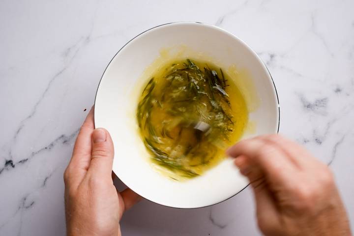 Garlic, rosemary, honey, lemon juice, and chicken broth being stirred together in a bowl.