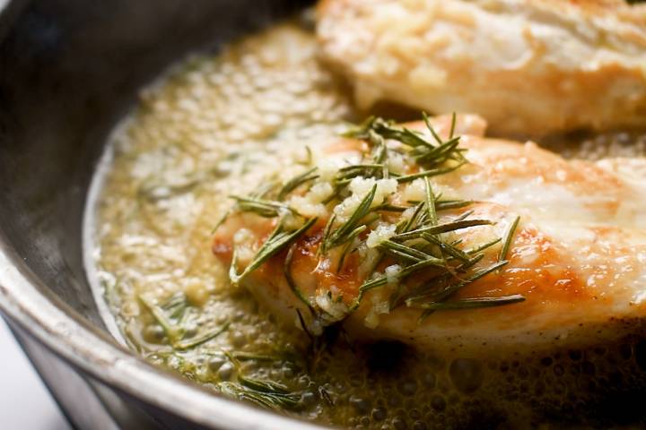 Chicken being cooked in a rosemary pan sauce in a cast iron skillet.