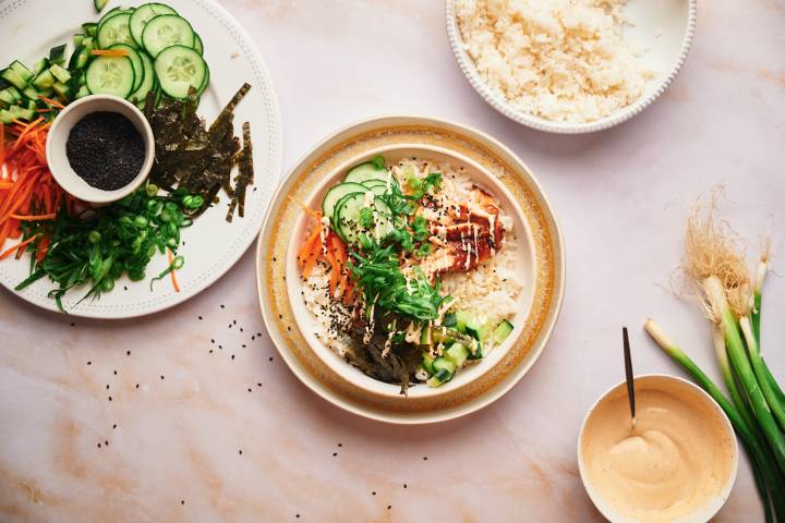 Salmon sushi bowls being assembled with baked salmon, rice, and seaweed.