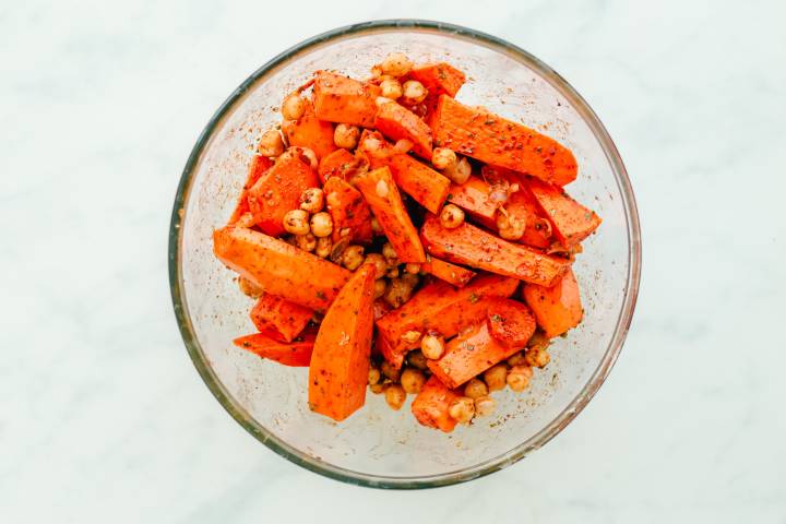 Sweet potatoes, carrots, and chickpeas in a bowl with olive oil and spices.