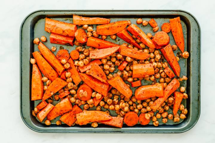 Sweet potatoes, carrots, and chickpeas spread out on a baking sheet.