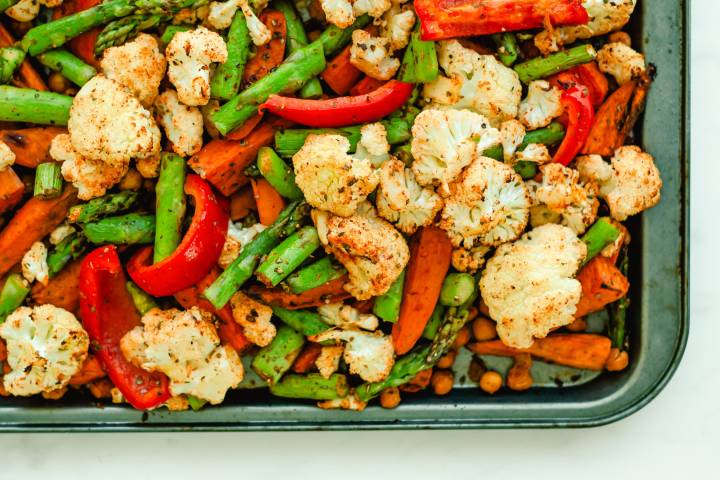 Cook chickpeas and vegetables on a baking sheet including cauliflower, red peppers, aspaagus, sweet potatoes, carrots, and chickpeas.