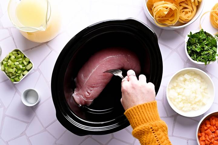 Turkey breast being placed in a slow cooker.