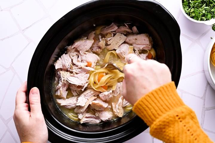 Turkey breast being added to a crockpot of turkey noodle soup.