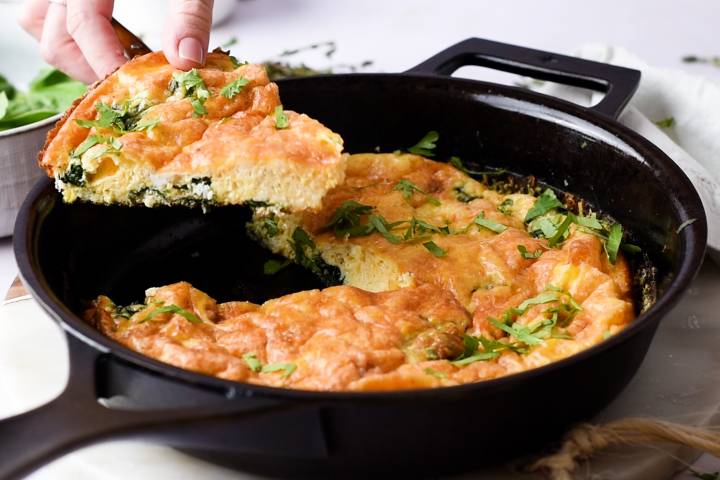 Slice of spinach frittata being picked up out of a skillet.