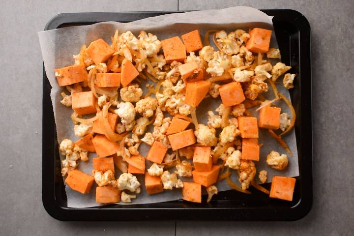 Sweet potatoes and cauliflower on a baking sheet with parchment paper.