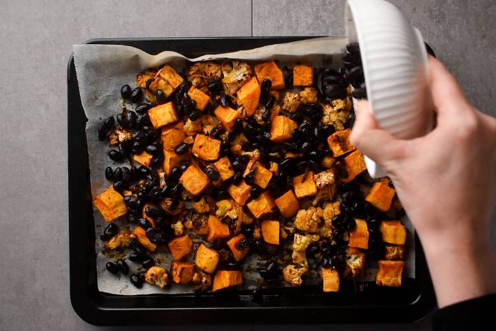 Black beans, sweet potatoes, and cauliflower on a baking sheet.