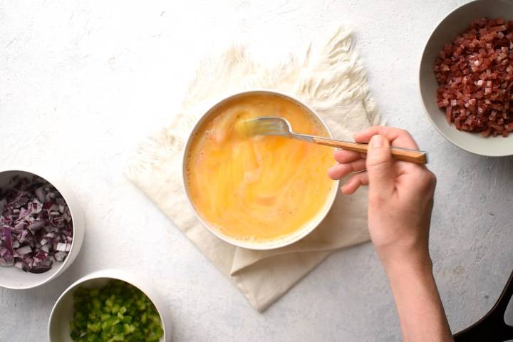 Eggs, milk, salt, and pepper being whisked in a bowl.