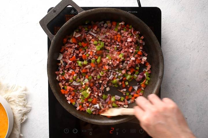 Diced ham, bell peppers, onions, and garlic cooking in a cast iron skillet.