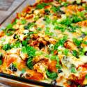 Chicken enchilada casserole with green onions and olives in a baking dish.