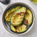 Grilled avocado halves drizzled with oil and sprinkled with pepper, served in a bowl beside coarse salt.