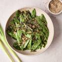 A finished dish of sauteed snow peas topped with sesame seeds in a beige bowl.