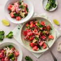 Watermelon, feta, and mint salad served in three bowls with sliced red onion, crumbled feta, cubed watermelon, and lime juice.