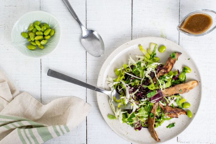 Chinese Chicken Salad with sesame dressing, chicken, edamame, and cabbage on a plate with a fork and spoon.
