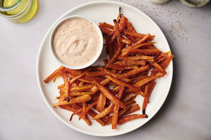 A bowl of baked carrot fries on a parchment-lined baking sheet.